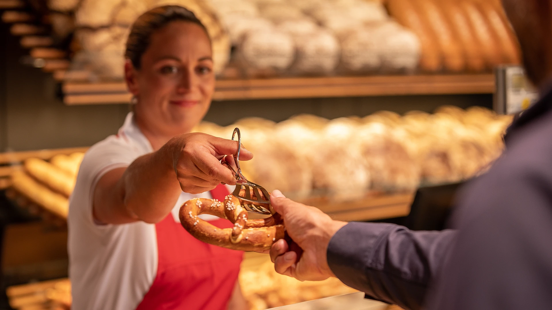 Verkäuferin reicht einem Kunden eine Breze über die Theke – Coverbild des Imagefilms für das Backhaus Hackner.
